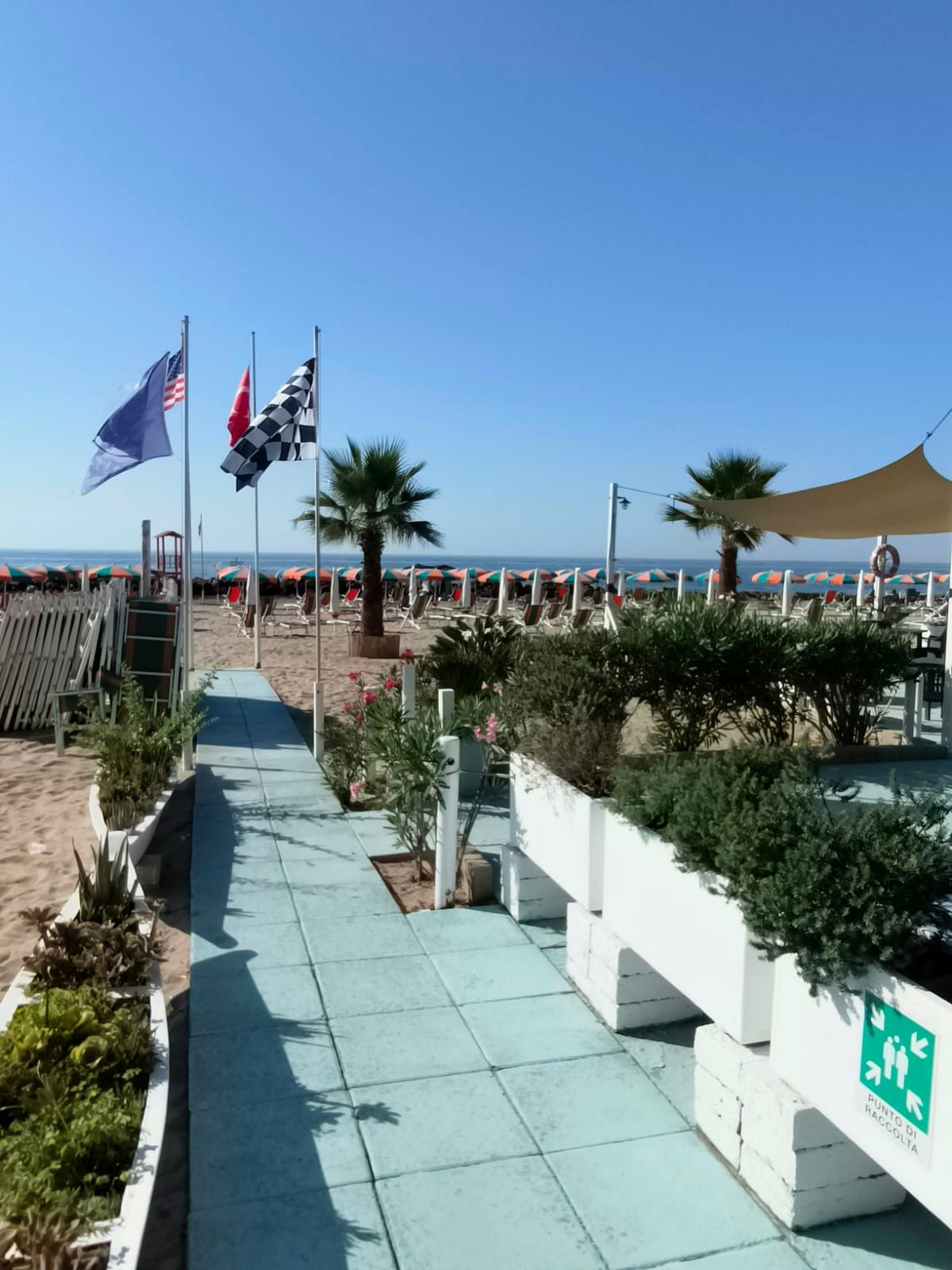 La passerella turchese verso il mare, con le bandiere e le palme